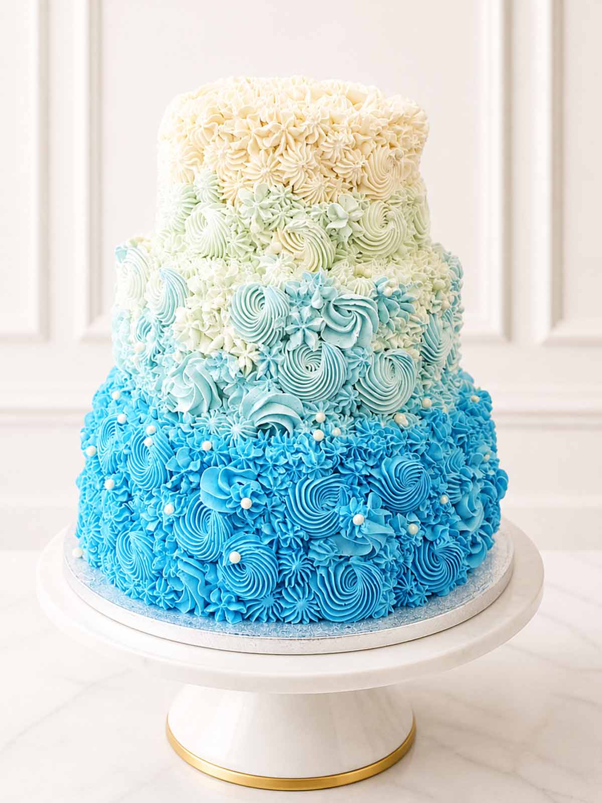 Contemporary elegant tiered wedding cake featuring an ivory to blue dip-dyed gradient Swiss meringue buttercream finish, studded with delicate white chocolate pearls. Delivered across Surrey.
