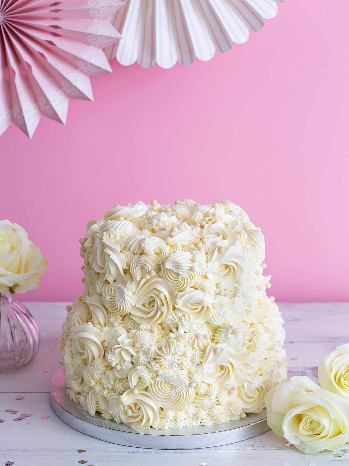 Two-tiered white cake with buttercream rosettes and sprinkles on a silver cake stand