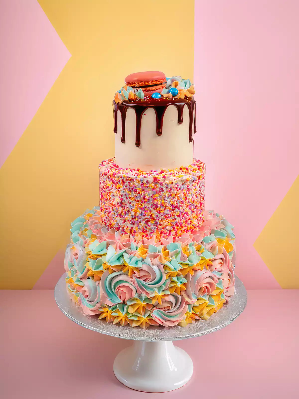 Three-tier birthday cake with chocolate drip, sprinkles and pastel rosettes