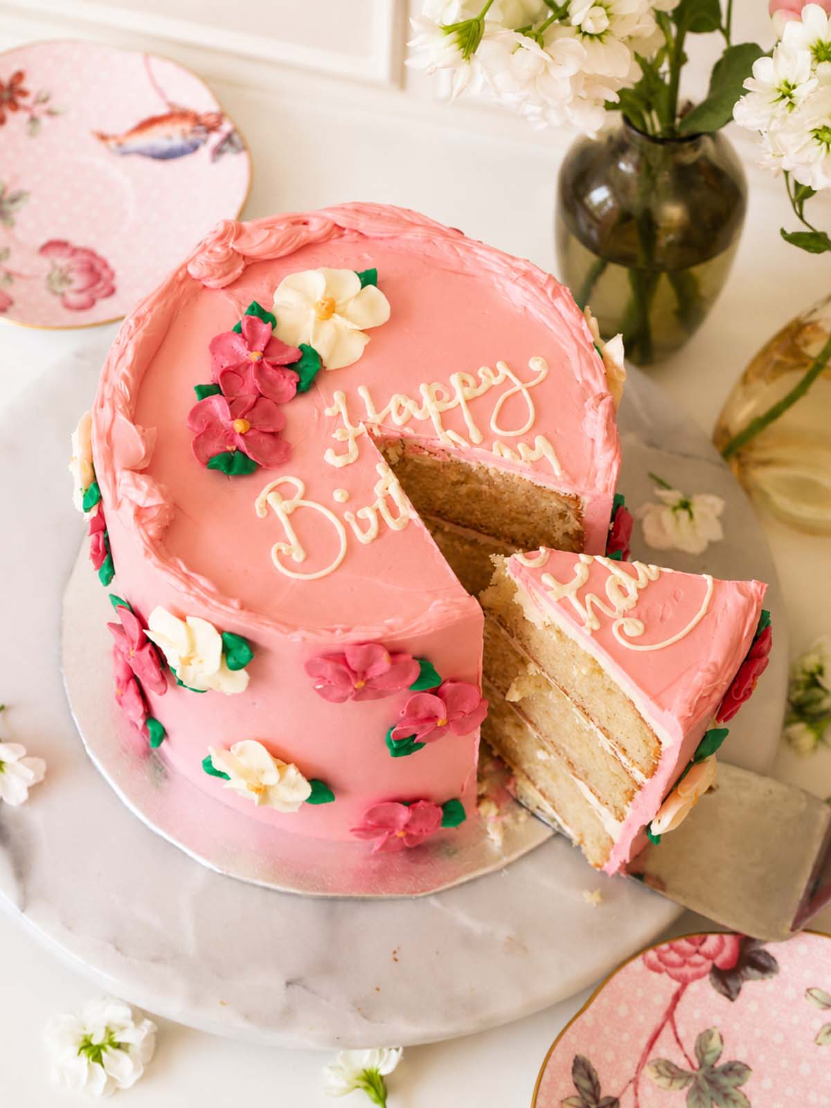 Pink birthday cake with floral buttercream decorations with a slice cut