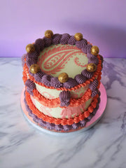 Two-tier cake with light green icing, orange and purple ruffles, and gold spheres