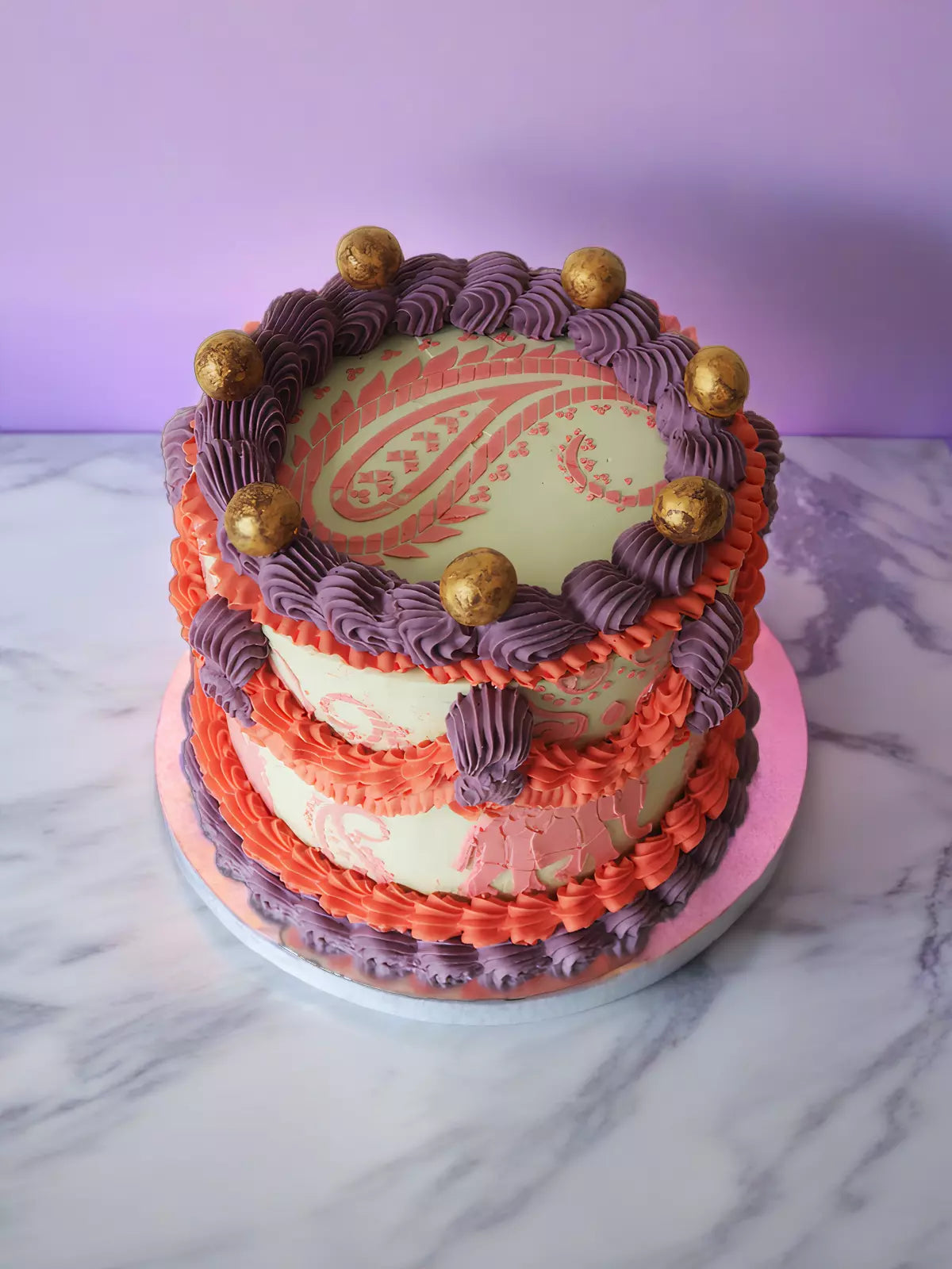 Two-tier cake with light green icing, orange and purple ruffles, and gold spheres