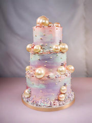 Three-tier cake with pastel watercolor frosting, edible pearls, and small white sprinkles
