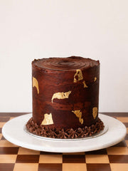 Chocolate cake with gold leaf decoration on a white marble cake stand