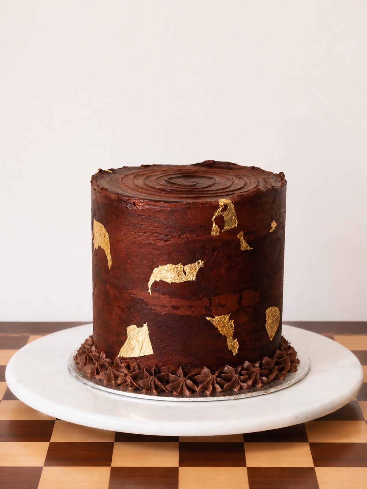 Chocolate cake with gold leaf decoration on a white marble cake stand