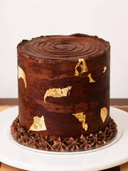 Chocolate cake with gold leaf decorations on a white plate with Next and Same Day