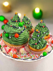 Christmas Tree Cake: Vanilla sponge cupcakes decorated with green frosting to look like Christmas trees, topped with stars, sprinkles, and candies, and served on a plate surrounded by festive sprinkles, meringues, and extra candies.