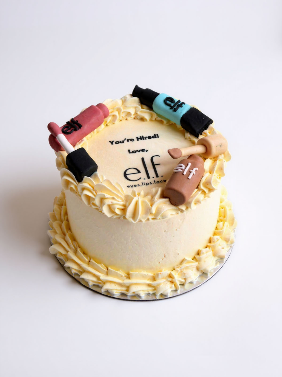 Corporate cake with 'elf' makeup products on top against a white background