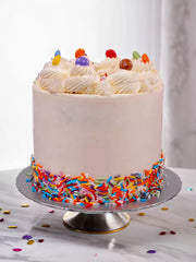 White frosted cake with colorful sprinkles around the base and candy on top