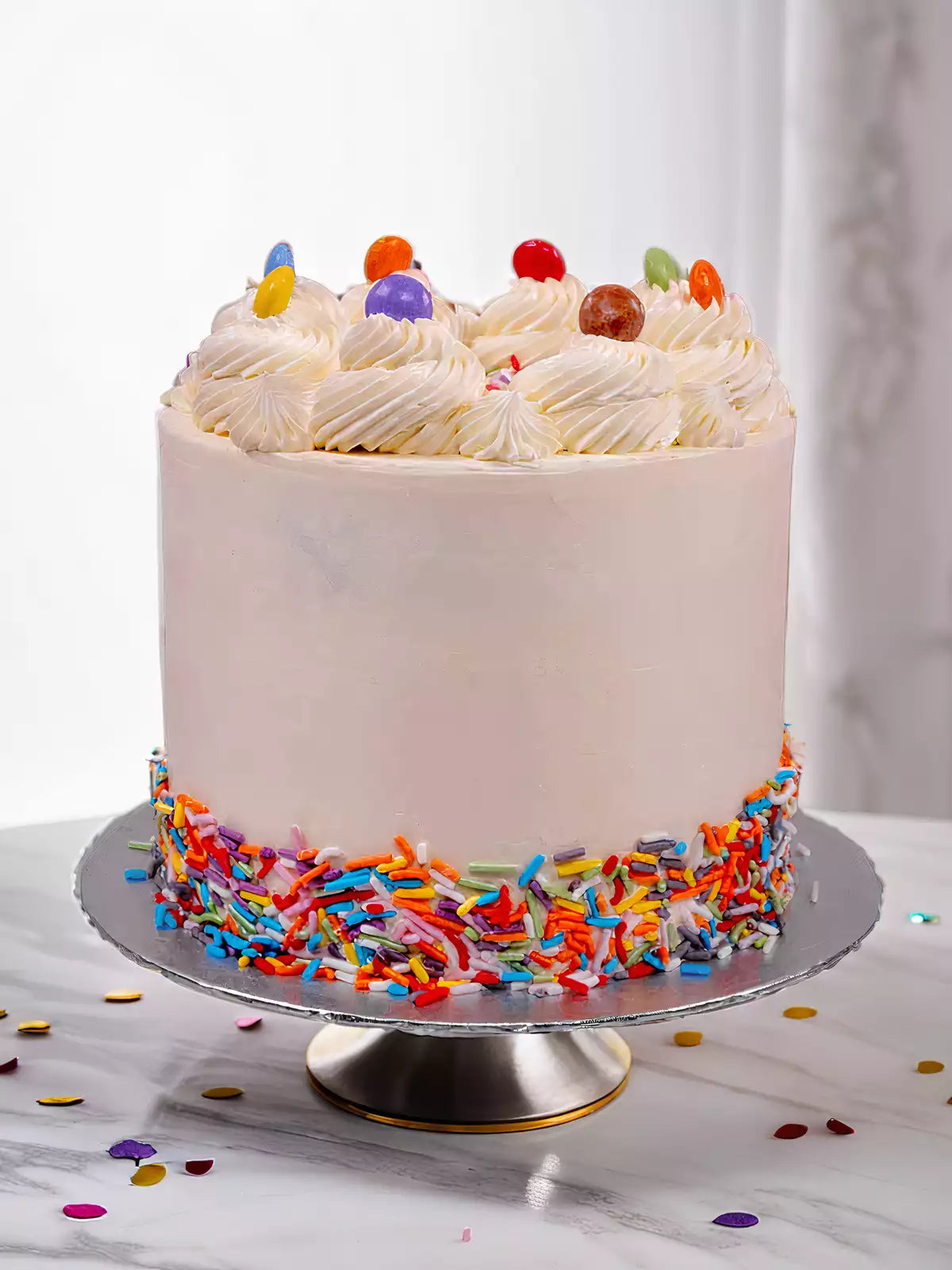 White frosted cake with colorful sprinkles around the base and candy on top
