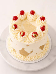 Decorative cake with white frosting, red cherries, and gold accents on a marble surface. Made and delivery in London  (M25) and Surrey UK