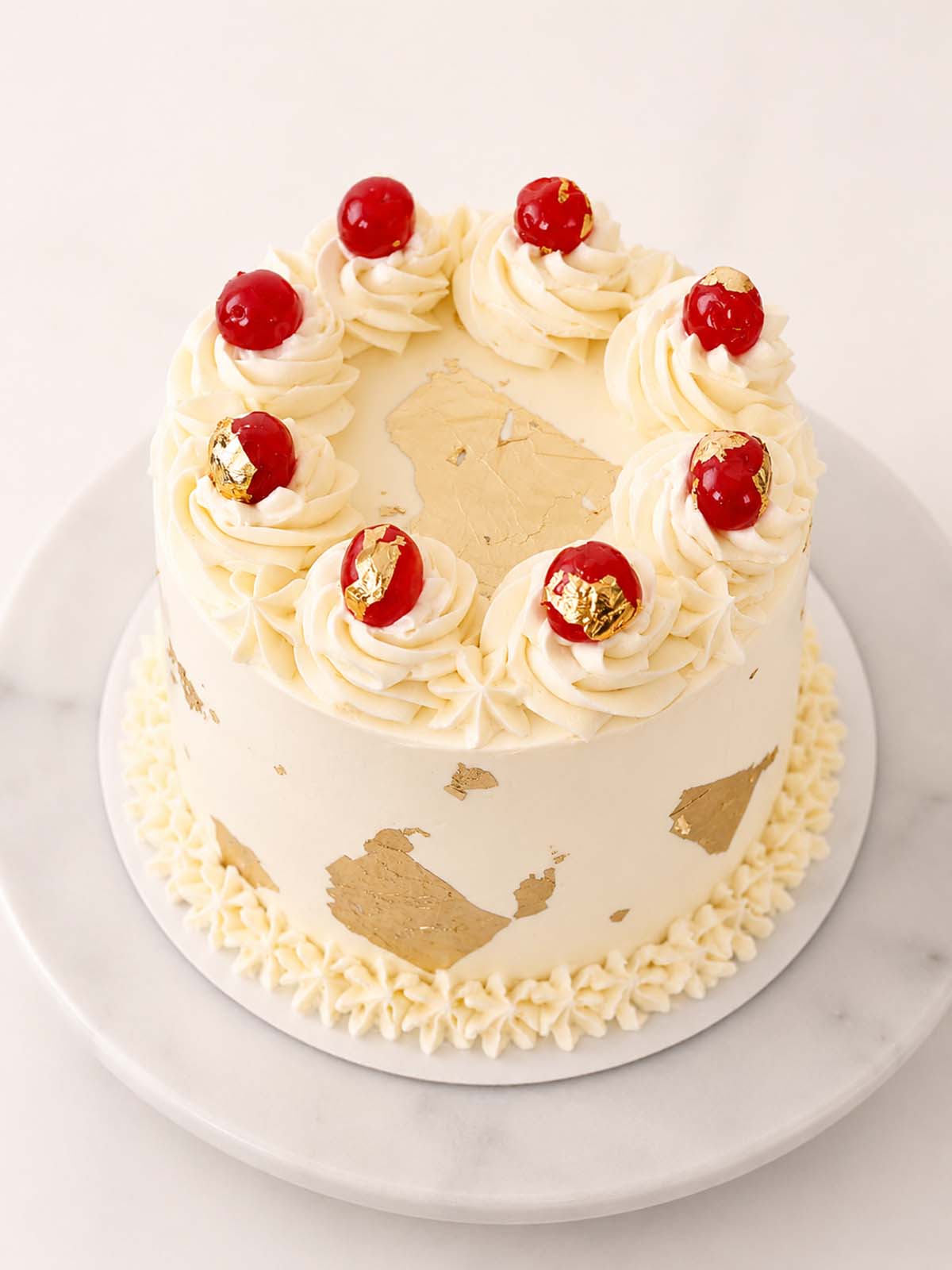 Decorative cake with white frosting, red cherries, and gold accents on a marble surface. Made and delivery in London  (M25) and Surrey UK
