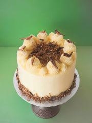 The Insect Cake features yellow frosting, swirls of icing, dried crickets, and mealworms, presented on a cake stand with a green background.