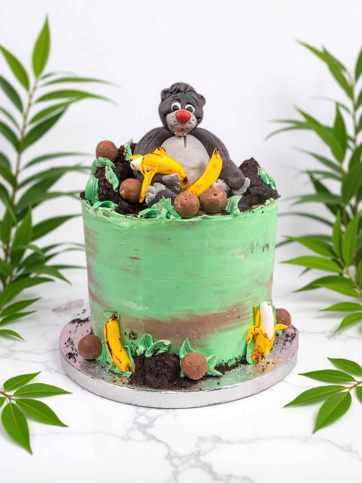 Jungle Book Baloo cake with green and brown icing, chocolate balls, and banana decorations