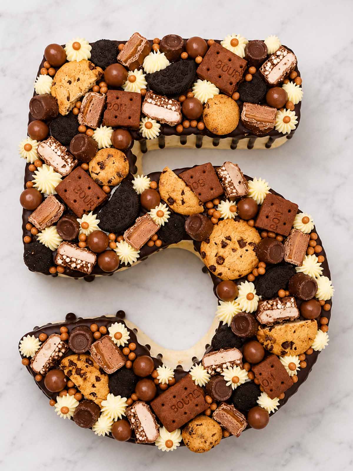 Number 5-shaped cake decorated with various cookies and candies on a marble surface delivered in London.