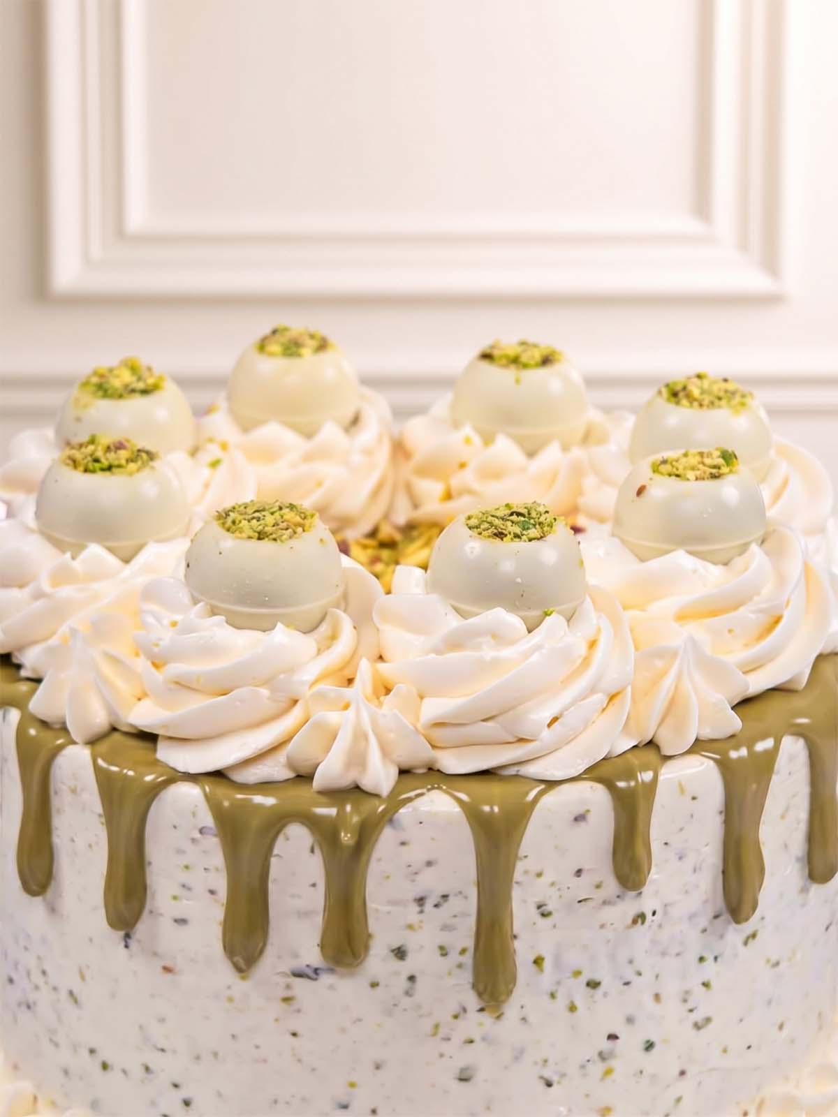 Close up of our Pistachio Truffle cake with white frosting, pistachio truffles, and crushed roasted pistachios, available for delivery in London (M25) and Surrey (UK). 