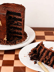 A chocolate cake with a slice removed, showing layers of cake and frosting, next to a slice on a plate