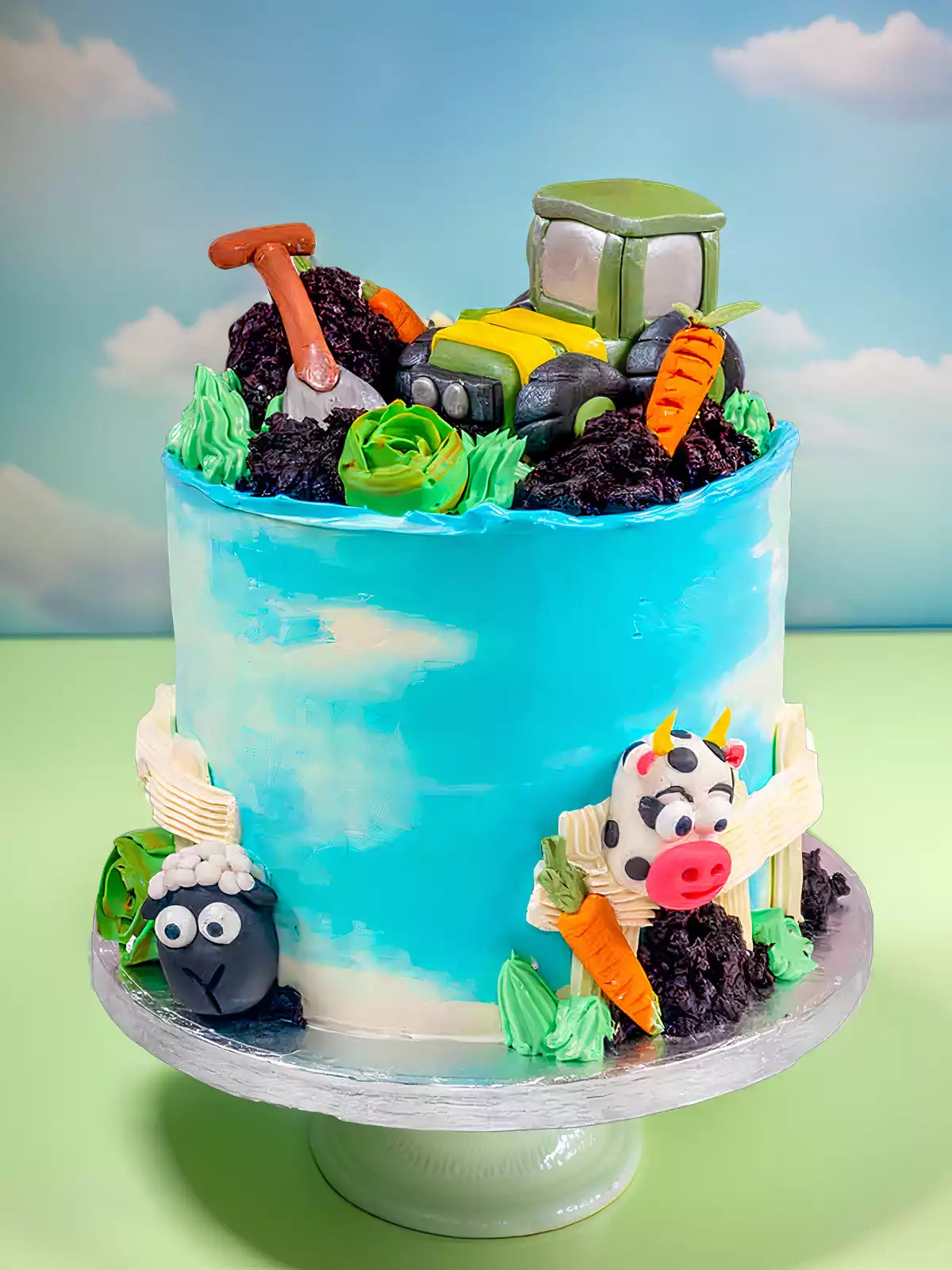 Farm themed cake with a tractor, carrots, a shovel, a sheep, and a cow