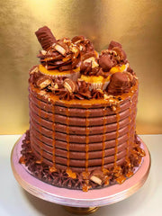 Chocolate cake with caramel drizzle, topped with cupcakes and chocolate bars