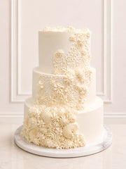 Three-tiered vintage lace wedding cake with intricate white floral designs