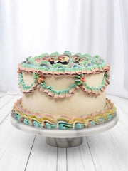 Round cake with pastel pink, blue, green, and yellow ruffles on a white marble cake stand