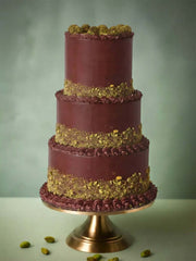 A bespoke three-tier dark chocolate wedding cake featuring textured pistachio crumb bands and decorative piping, displayed on a gold stand for a London wedding.