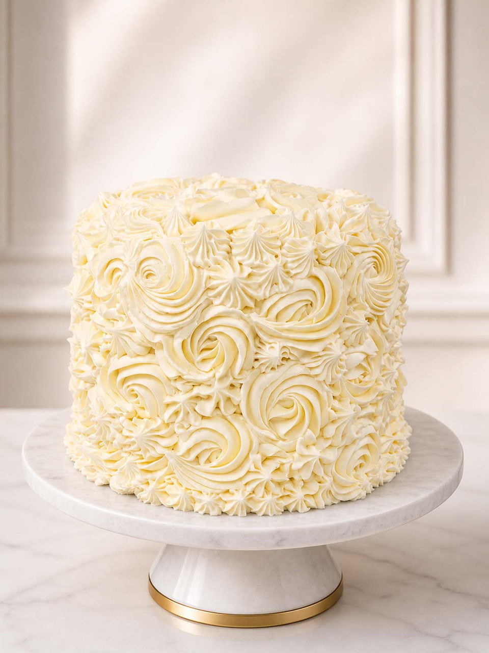 Elegant ivory birthday cake featuring smooth vanilla Swiss meringue buttercream and hand-piped swirls, concealing five secret buttermilk rainbow sponge layers inside. Delivered across London and Surrey.