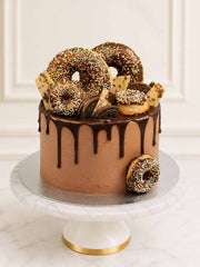 A decadent chocolate and doughnut celebration cake featuring chocolate-glazed buttermilk doughnuts, golden Oreos, and white chocolate shards dusted with gold lustre, delivered in London.