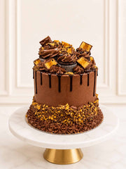 Indulgent three-layer chocolate sponge celebration cake frosted with chocolate Swiss meringue buttercream, topped with honeycomb chocolate bars, glossy Belgian chocolate drip, and mini cupcakes. Delivered in London.