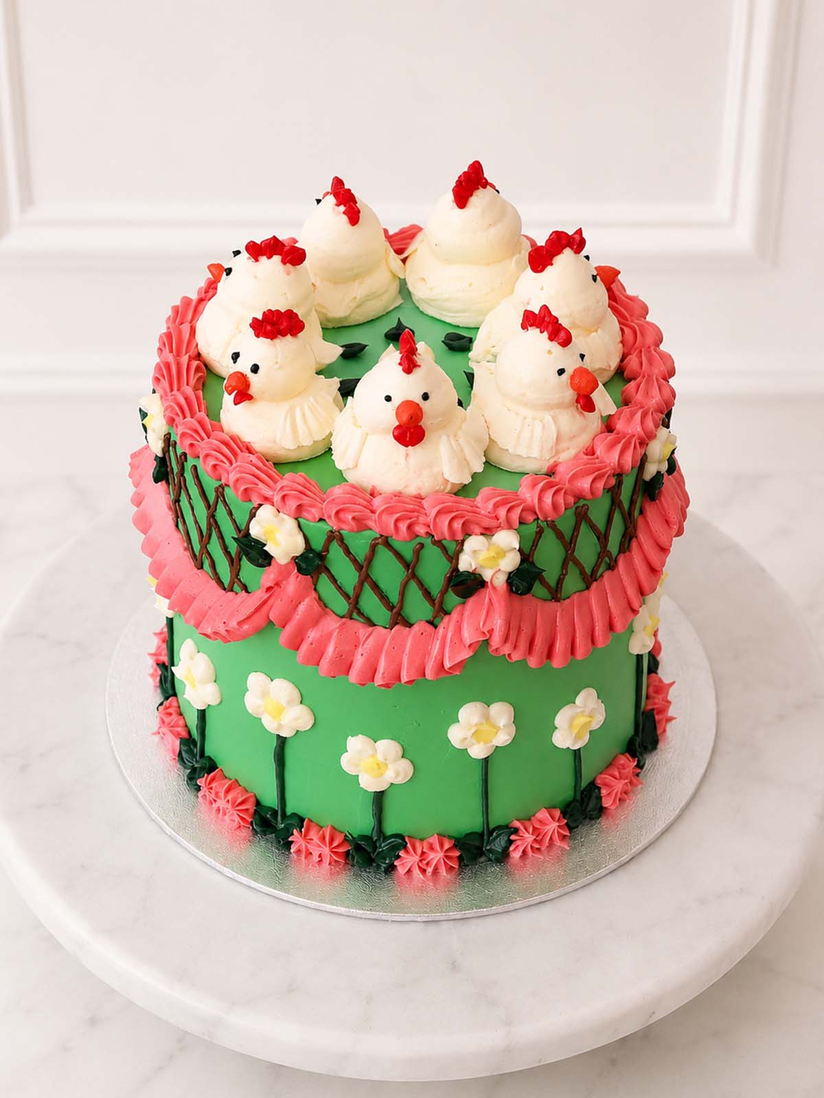 A round cake decorated with green icing, pink piped borders, small white flowers, and five white chick figures made and delivered in London and Surrey (UK)