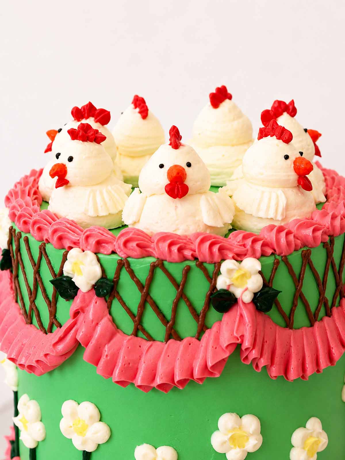 Close-up of hand-piped buttercream chickens on a green Belgian chocolate cake with pink ruffles and floral piping.