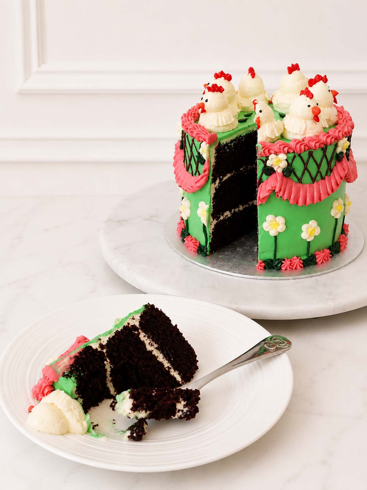 Kitsch Chicken Cake with a slice removed, showing Belgian chocolate sponge layers and vanilla Swiss meringue buttercream.