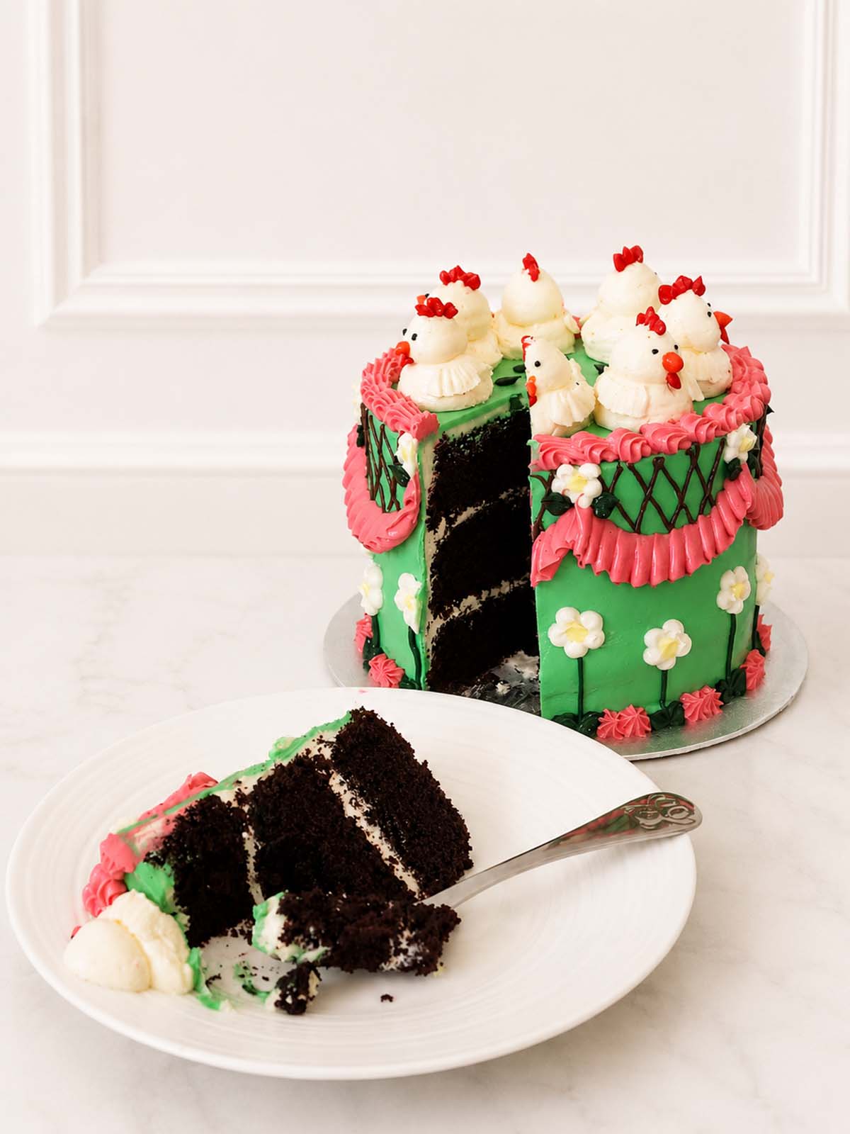 Slice of Kitsch Chicken Cake showing rich Belgian chocolate sponge, green buttercream, pink piping and creamy vanilla filling.