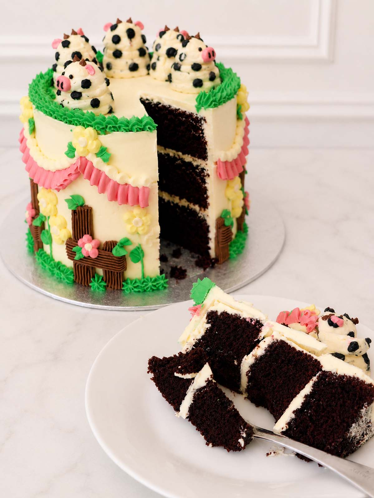 Kitsch Cow Cake with a slice removed, showing rich Belgian chocolate sponge layers and vanilla Swiss meringue buttercream.