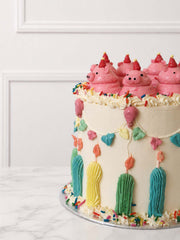 Kitsch celebration cake decorated with hand-piped pink buttercream pigs, party hats, bunting, balloons, candles and rainbow sprinkles.