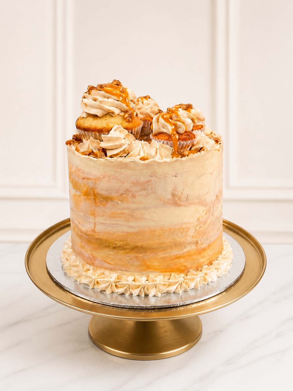 A luxurious banoffee celebration cake featuring small-batch banana sponge, salted caramel ganache, and Swiss meringue buttercream topped with artisan cupcakes and toffee fudge, delivered across London and Surrey.