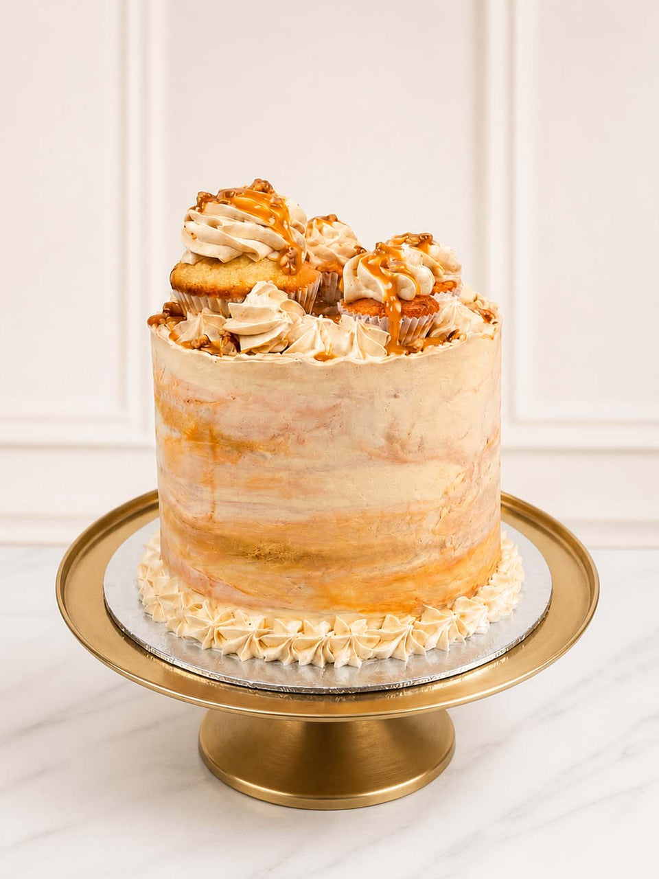 A luxurious banoffee celebration cake featuring small-batch banana sponge, salted caramel ganache, and Swiss meringue buttercream topped with artisan cupcakes and toffee fudge