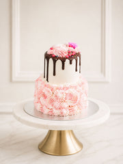 A mini two-tier Madagascan vanilla cake decorated with a Valrhona chocolate drip, pink and ivory hand-piped buttercream, and a delicate meringue kiss
