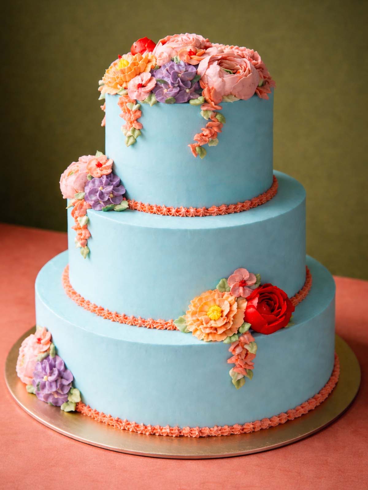 Close-up of the piped orange details and hand-crafted buttercream floral arrangements on a three-tier wedding cake.