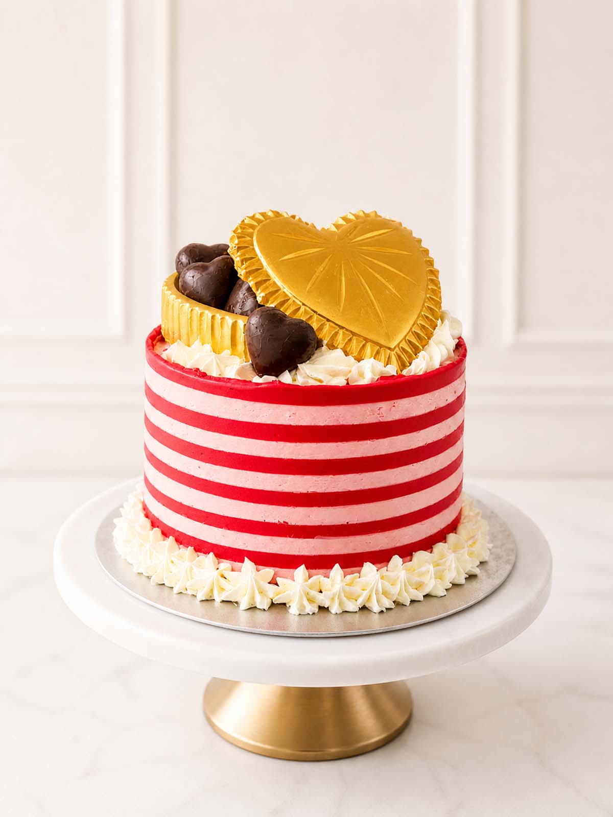 Romantic Valentine's Day or anniversary gift cake featuring fluffy vanilla sponge, pink and red striped Swiss meringue buttercream, and an edible golden chocolate box filled with heart-shaped caramels. Delivered in London.
