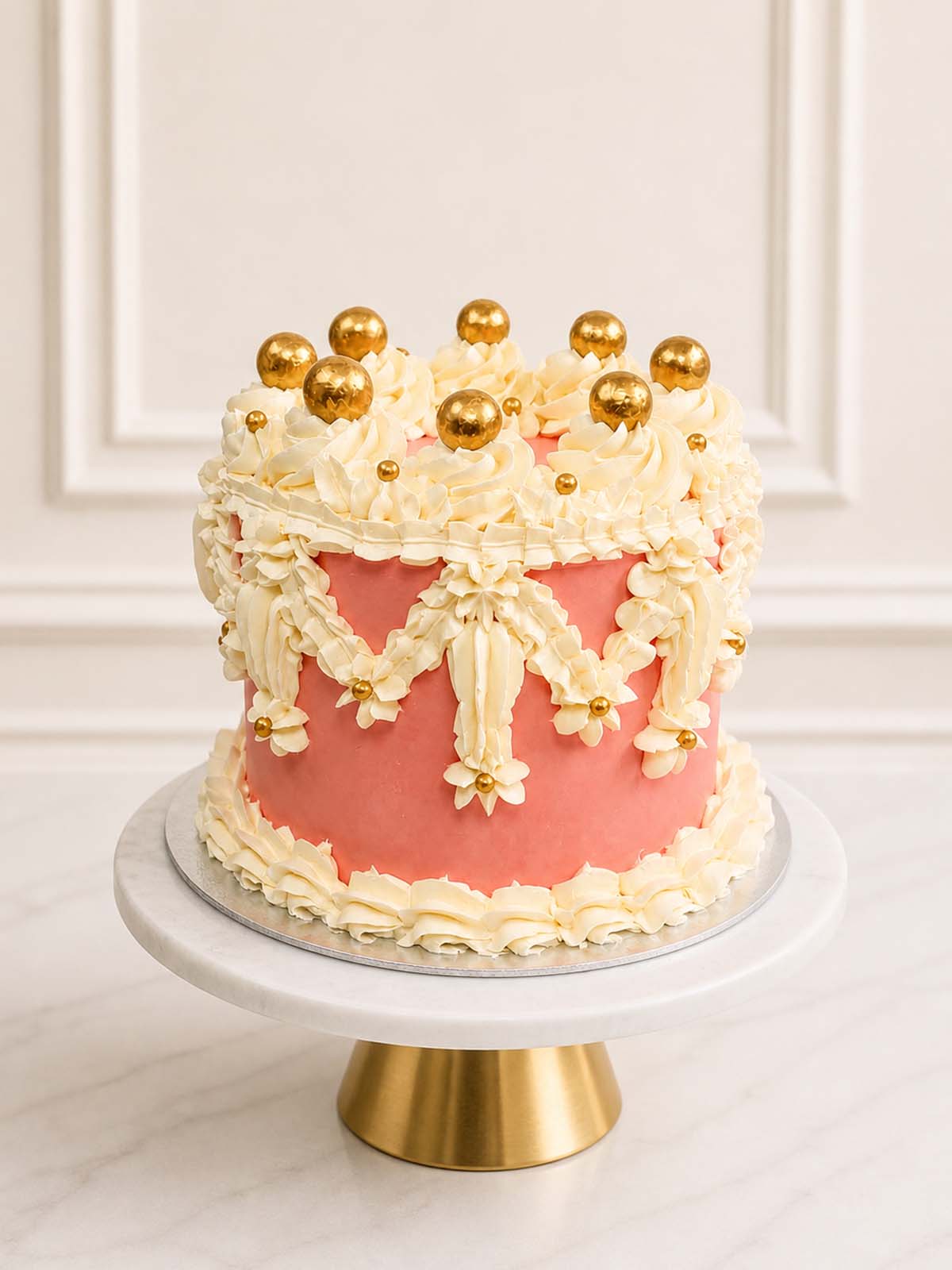 A majestic pink and ivory celebration cake inspired by Windsor Castle featuring three layers of vanilla sponge, intricate vintage buttercream piping, and golden chocolate pearls, delivered in London.