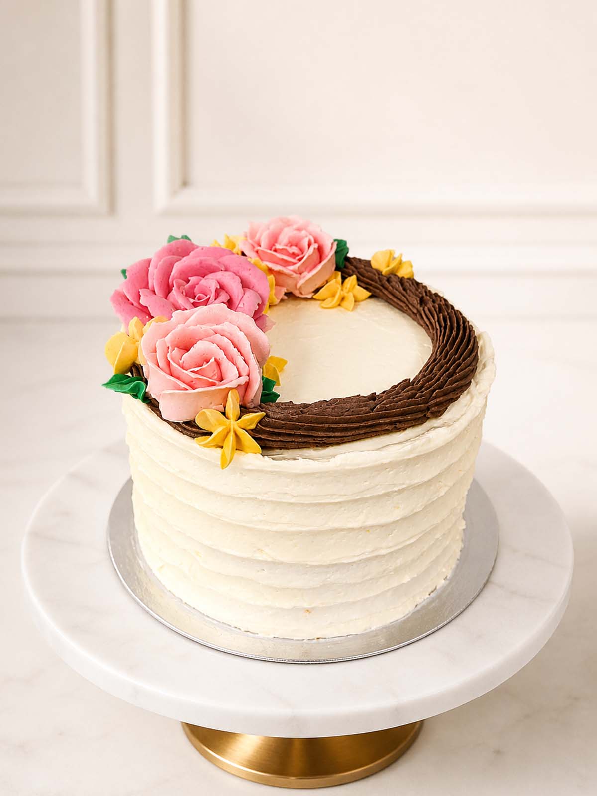A charming, cottagecore-inspired celebration cake featuring two layers of vanilla sponge finished with a rustic vanilla buttercream ruffle. Exquisitely detailed with a delicate, hand-piped buttercream floral wreath and dainty green foliage. Delivered in Richmond and across London.