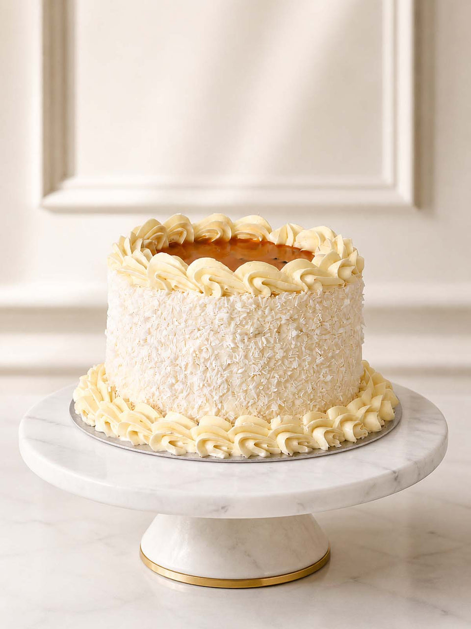 A tropical summer celebration cake featuring two layers of fluffy mango sponge baked with exotic fruit chunks, frosted in vanilla Swiss meringue buttercream, coated in desiccated coconut, and topped with a tangy mango and passion fruit coulis. Delivered in London.