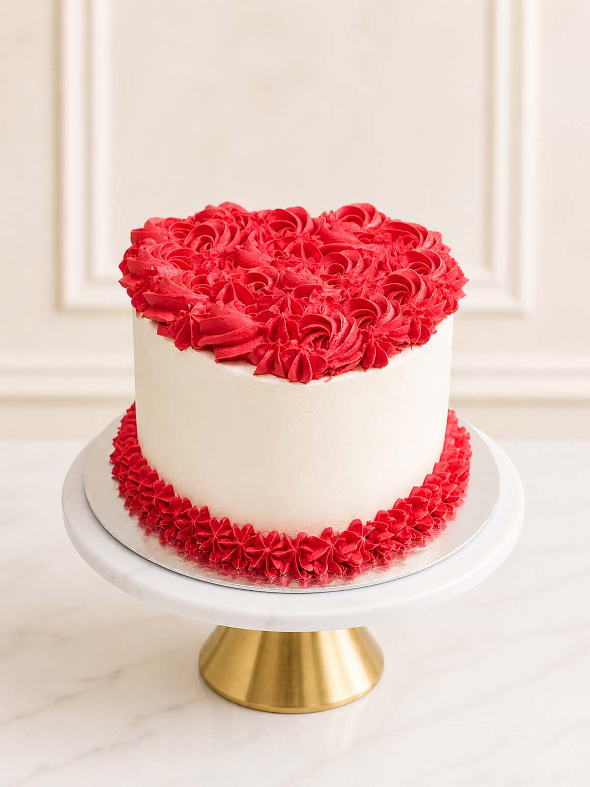 A romantic heart-shaped red velvet cake decorated with vintage-style red buttercream rosettes and smooth vanilla Swiss meringue buttercream, delivered in London.