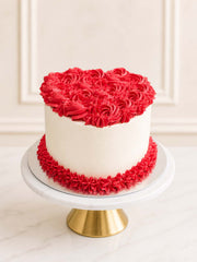A romantic heart-shaped red velvet cake decorated with vintage-style red buttercream rosettes and smooth vanilla Swiss meringue buttercream, delivered in London.