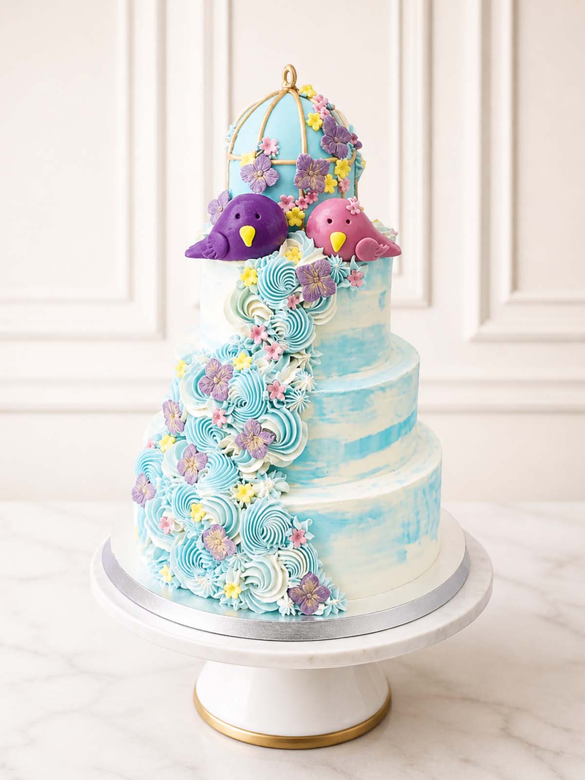 Whimsical romantic wedding cake featuring a serene blue watercolour buttercream finish, beautifully decorated with a gold-gilded birdcage, hand-modelled fondant love-birds, and delicate hydrangeas. Delivered across Surrey.